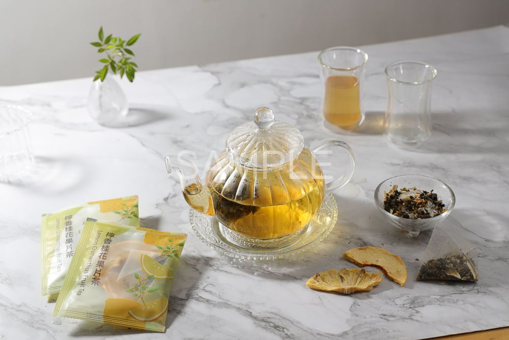 A plate holds dried tea leaves, a pyramid tea bag, steeped tea, and dried pineapple slices on a white marble background.