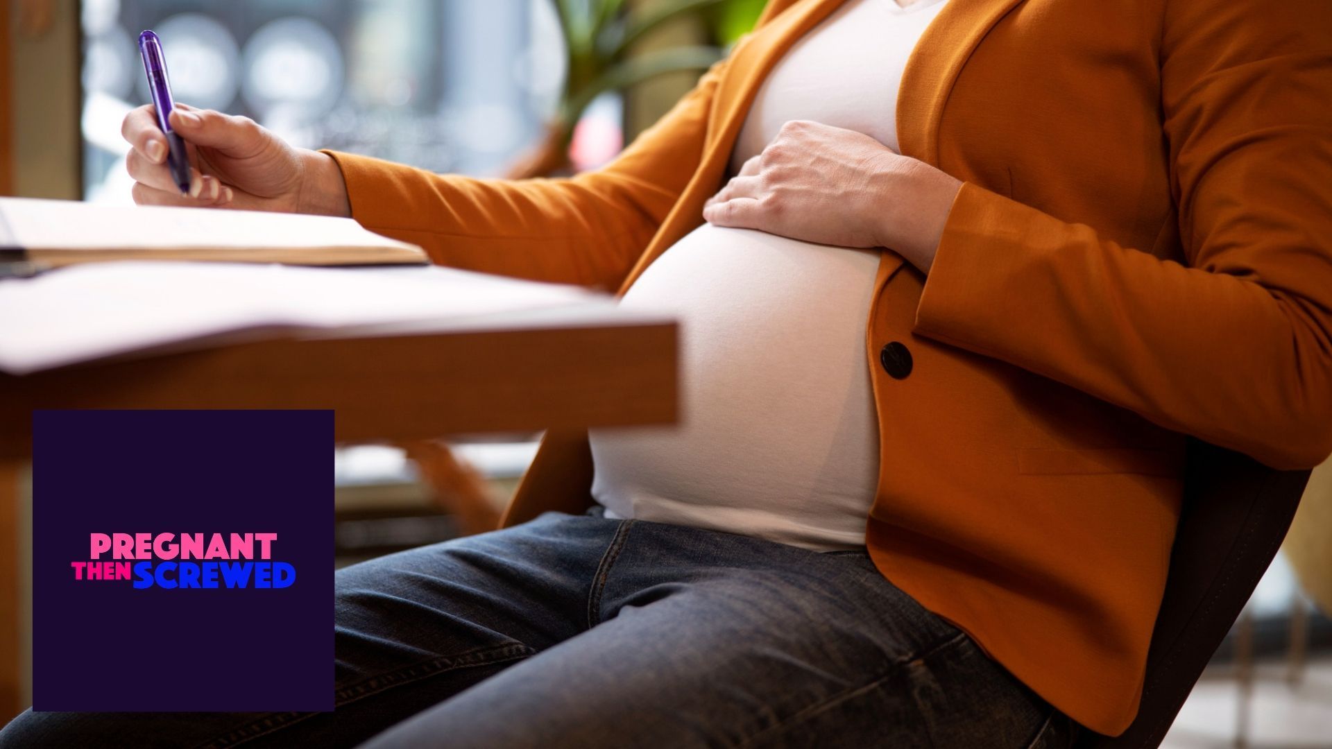 A pregnant woman is sitting at a table holding her belly.