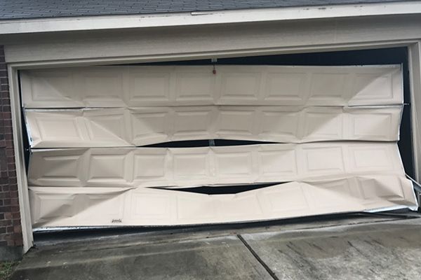 A broken garage door is sitting on the side of a house.