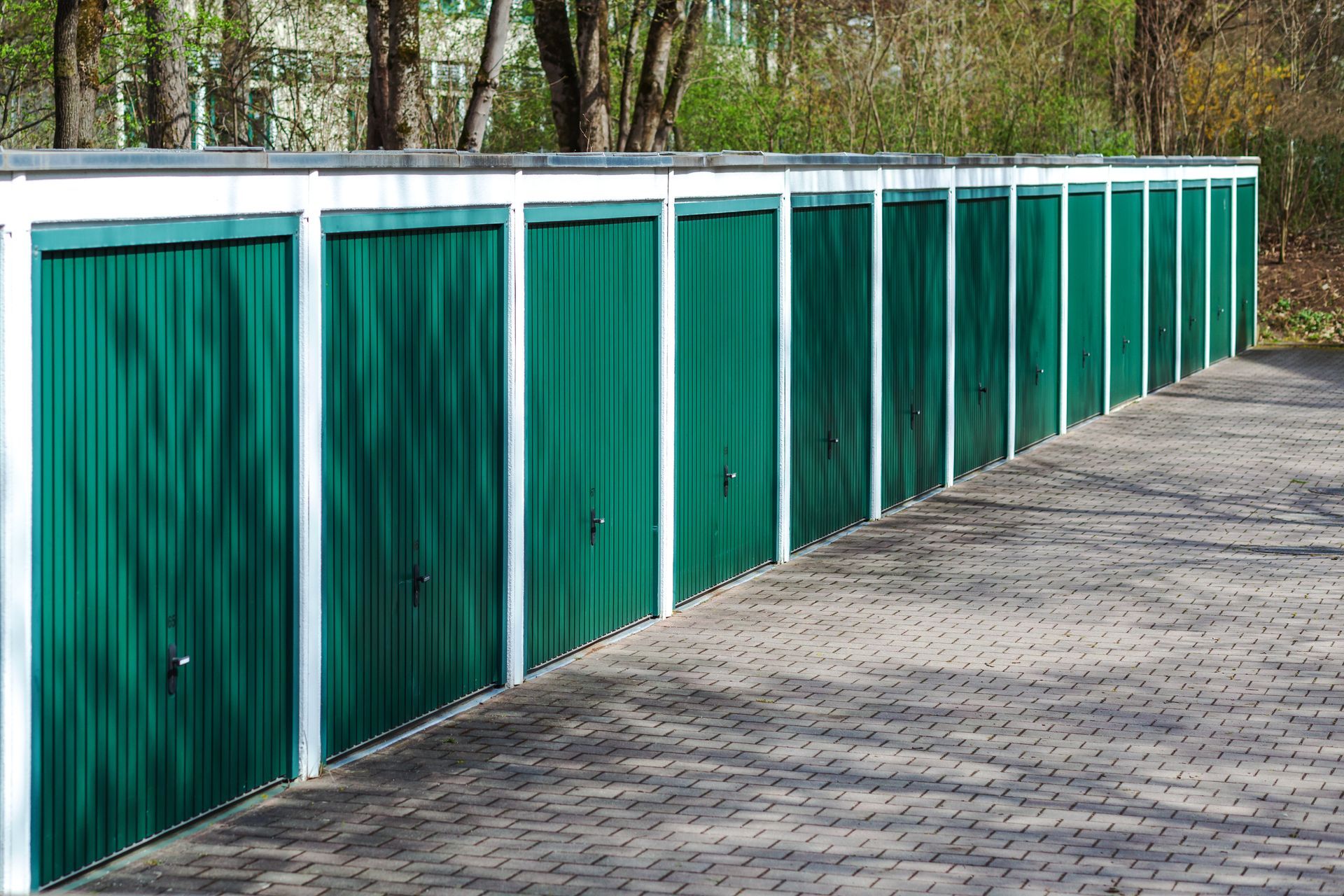 Row of green storage unit doors with white trim along a paved walkway.