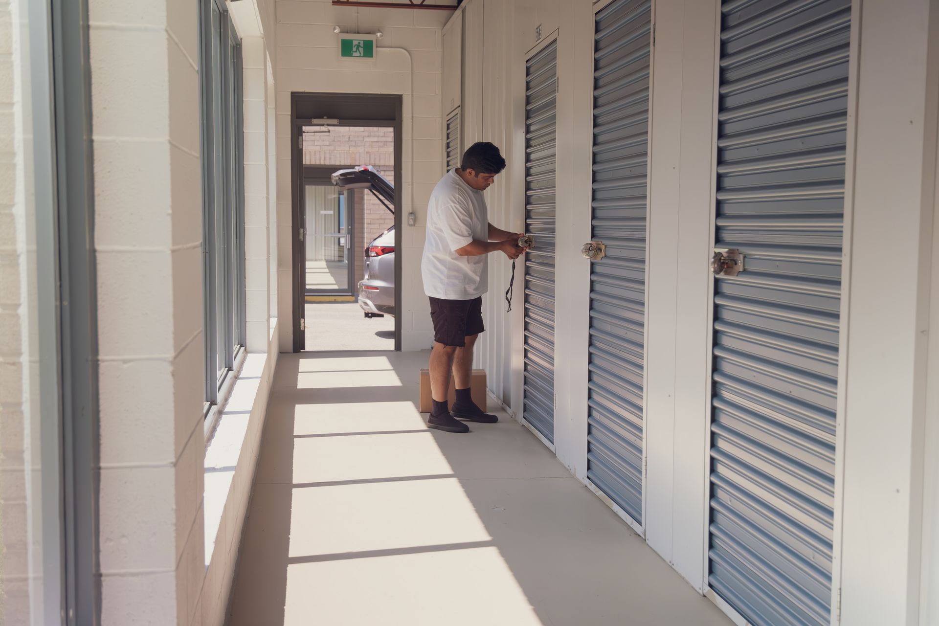 A man is standing in a hallway with blue storage units. He is working on a lock. A man is standing in a hallway with blue storage units. He is working on a lock.