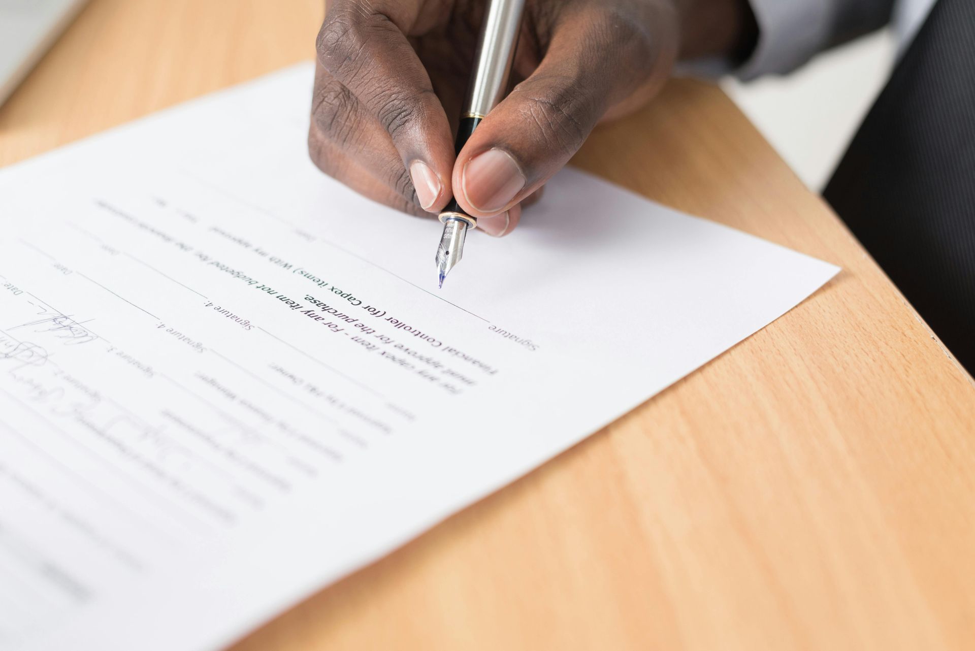 Hand signing a document on a wooden desk with a pen