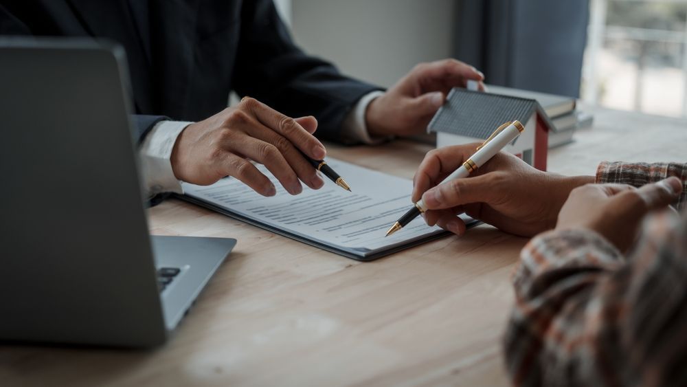 Business meeting with two people at a table, laptop, notebook, coffee cup, and gavel visible.