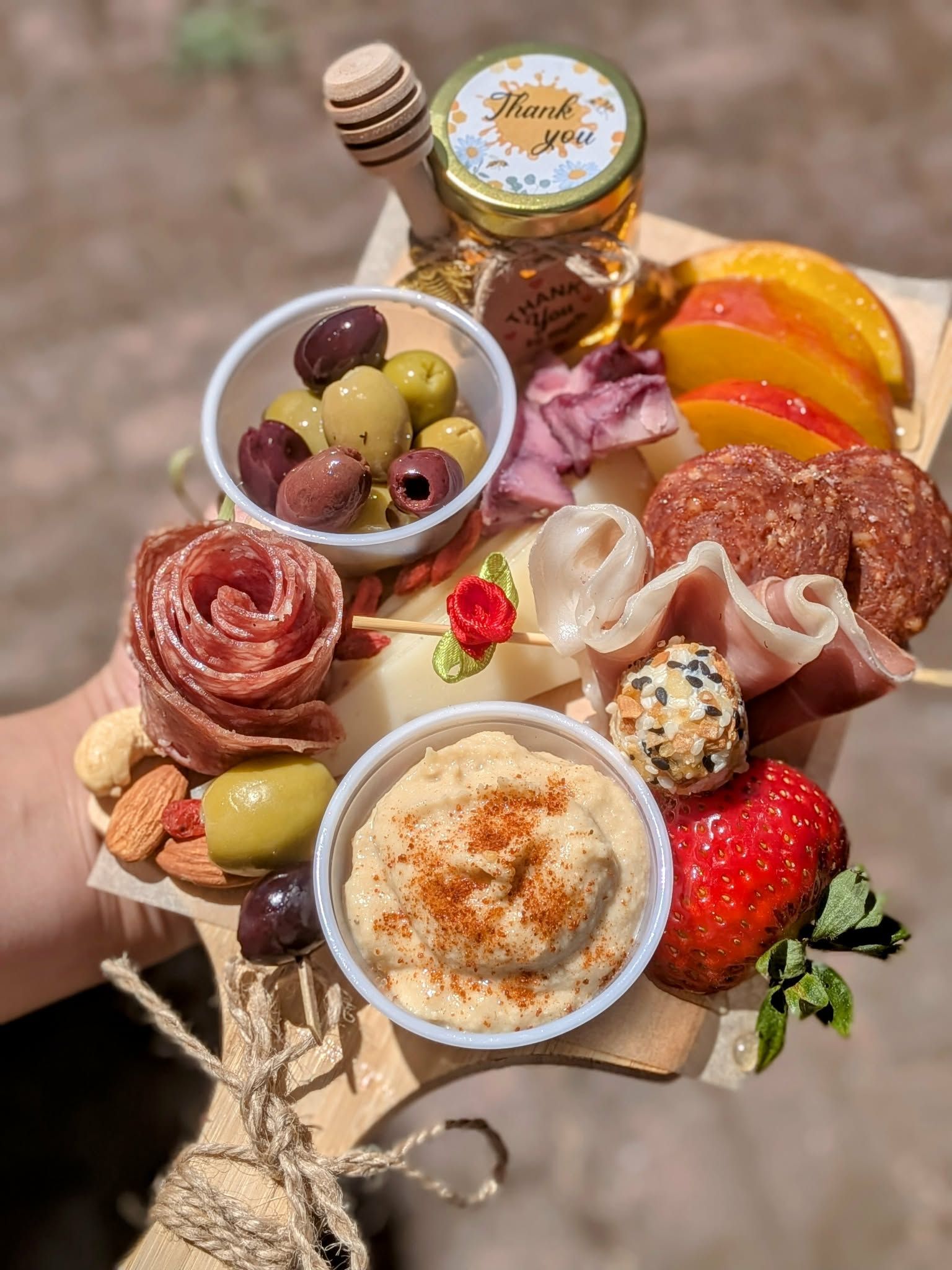 Charcuterie board with olives, hummus, cheese, fruit, and honey, held in a hand.