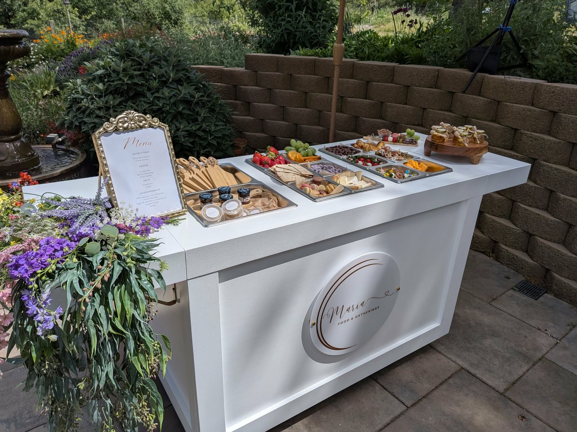 White outdoor food bar with charcuterie boards and floral decor.