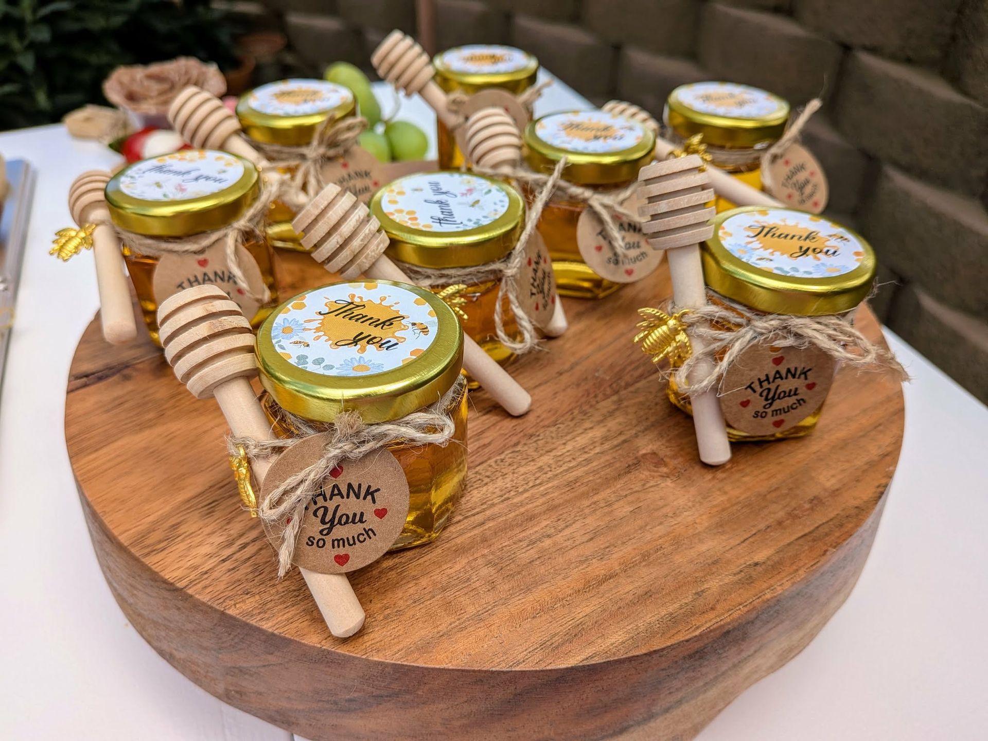 Small honey jars with wooden dippers and tags on a wooden cake stand, a party favor.