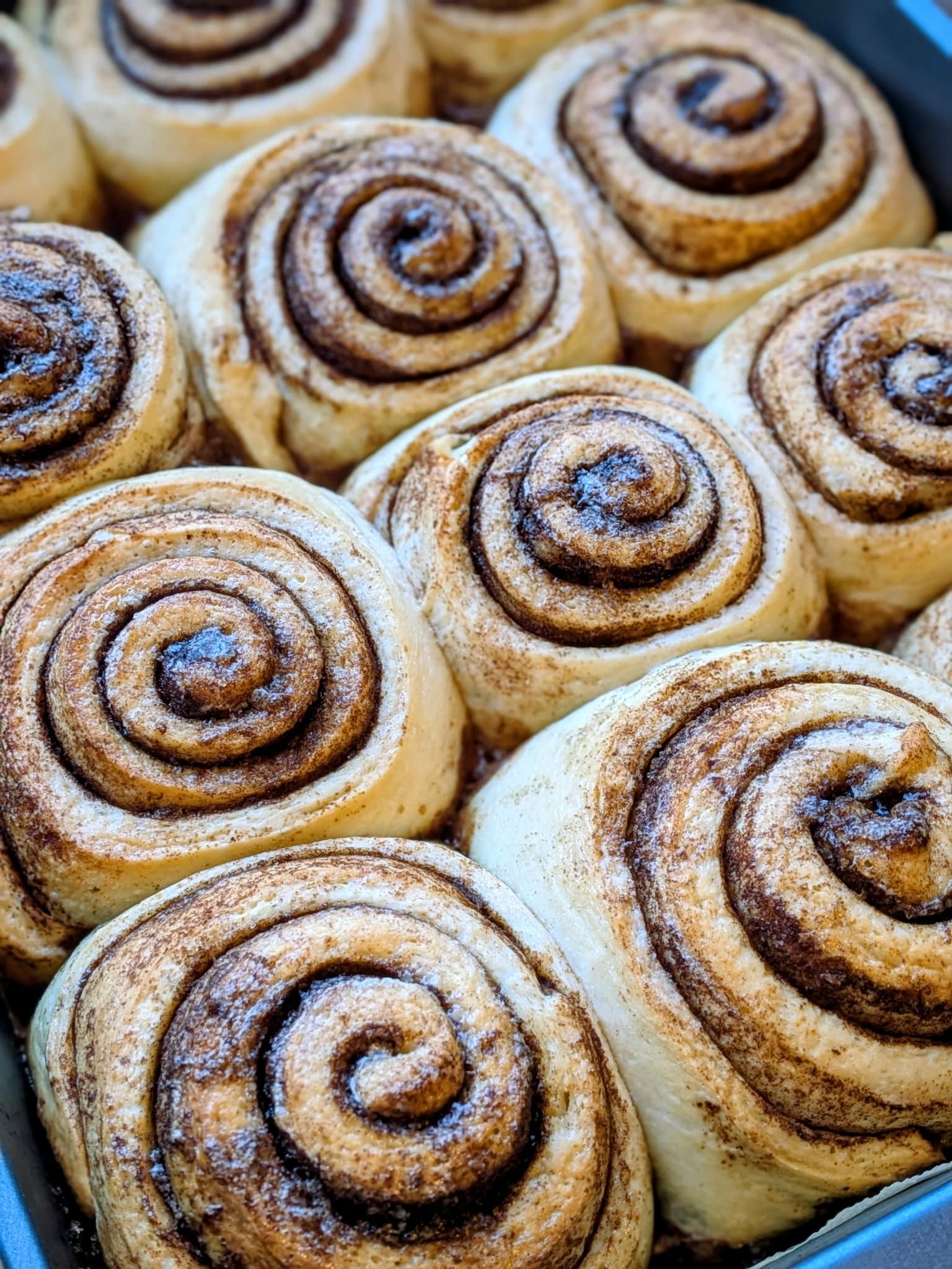 Close-up of a baking pan filled with golden-brown cinnamon rolls, swirled with cinnamon sugar.