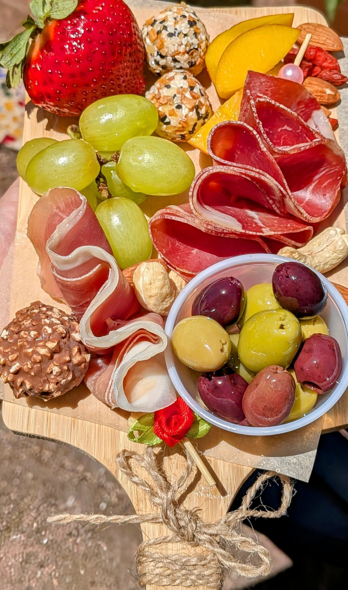 Charcuterie board with grapes, olives, cured meats, fruit, and cheese balls.