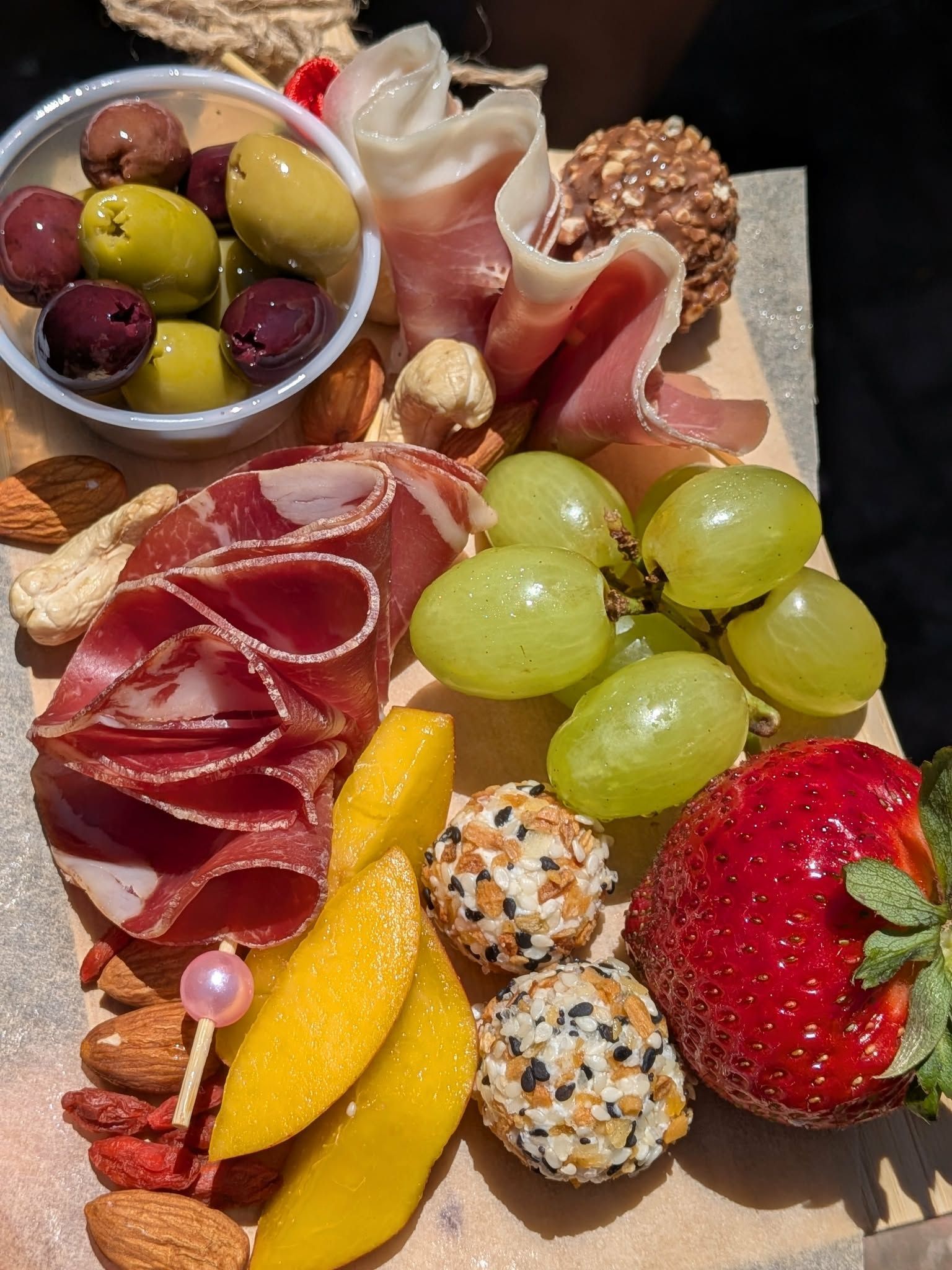 Charcuterie board: olives, grapes, meat, fruit, nuts, and cheese balls on wood.