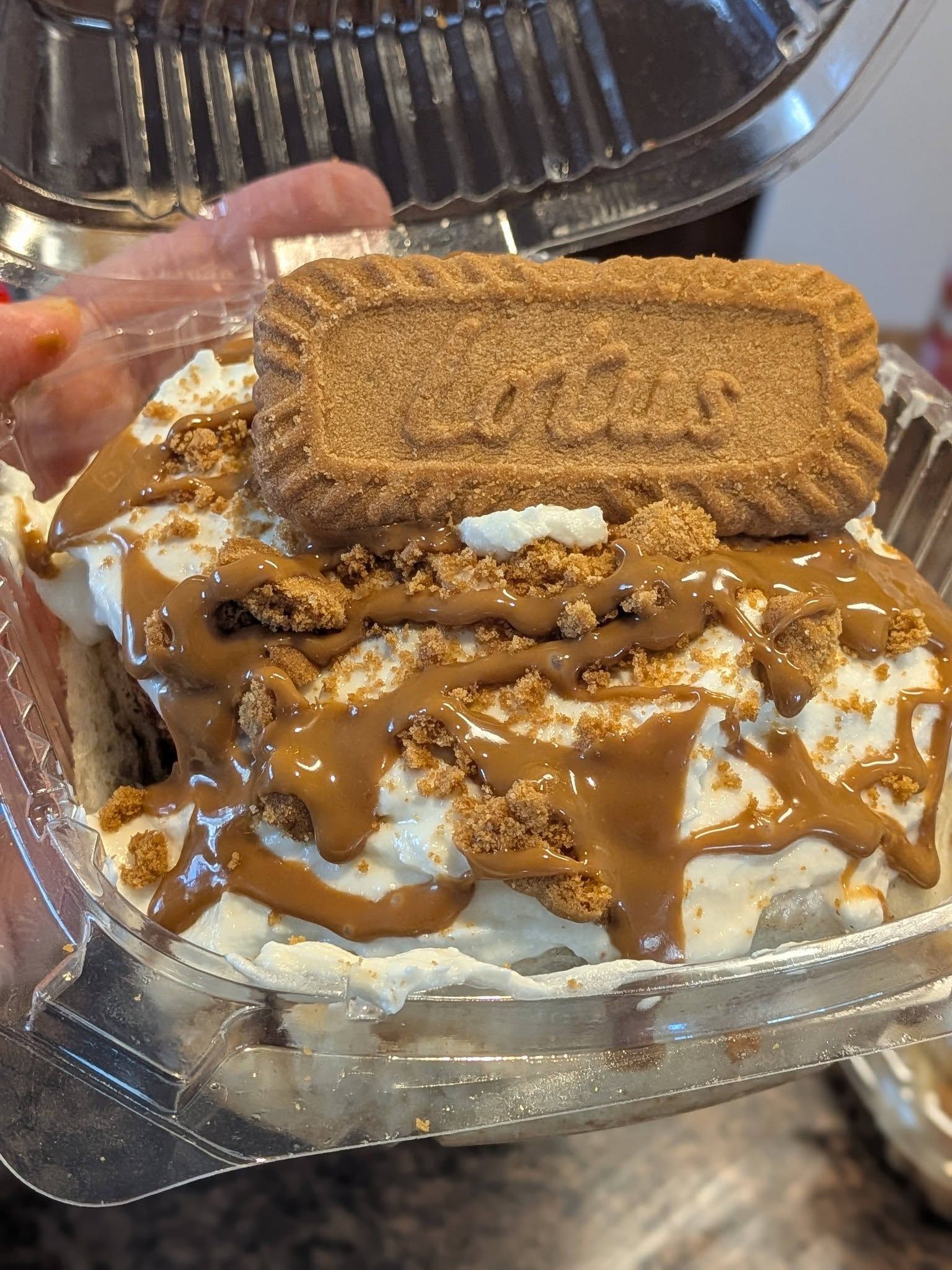 Dessert with white cream, brown sauce, crumbs, and cookie in a clear container.