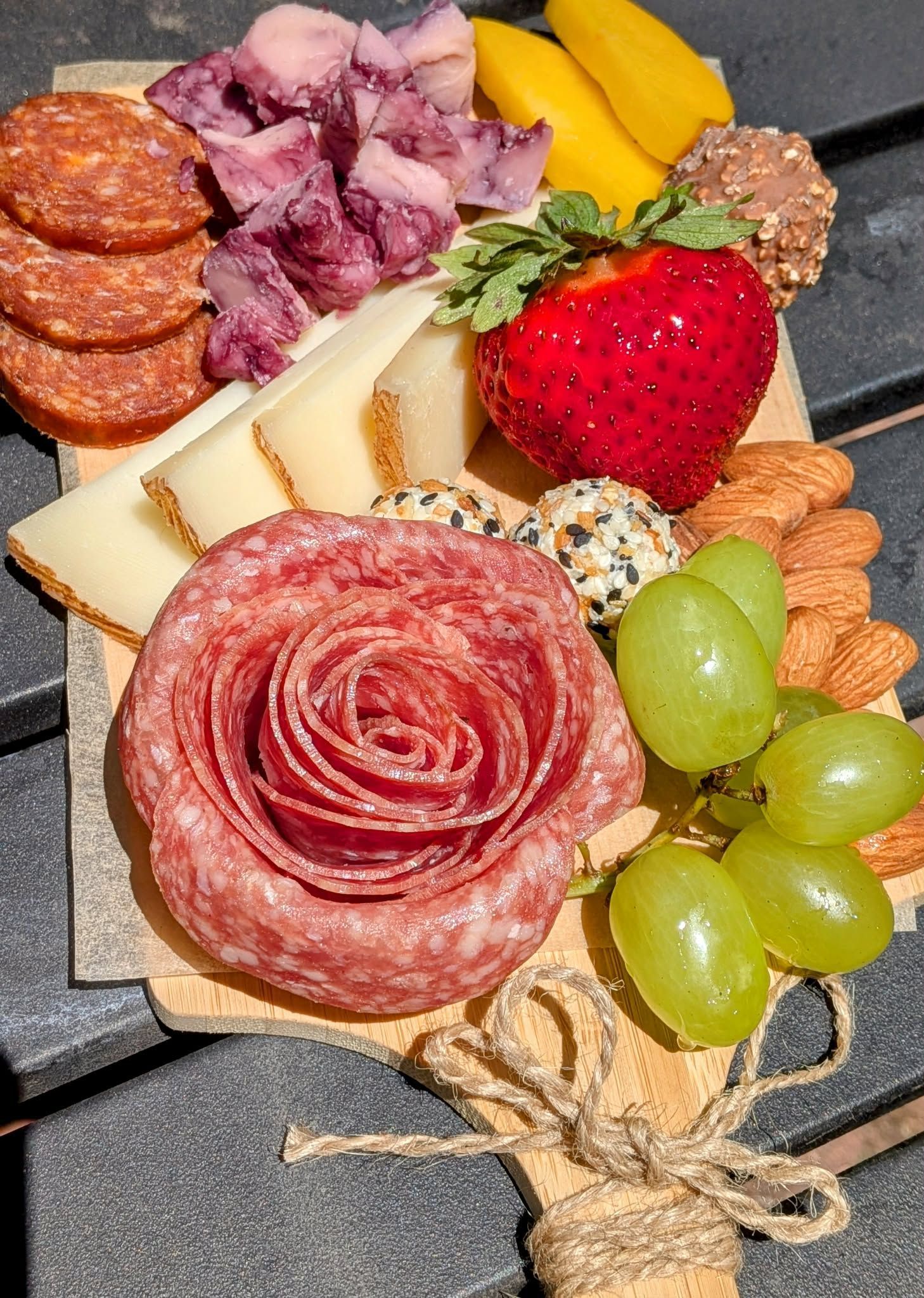 Charcuterie board with salami rose, cheeses, meats, grapes, nuts, fruit.