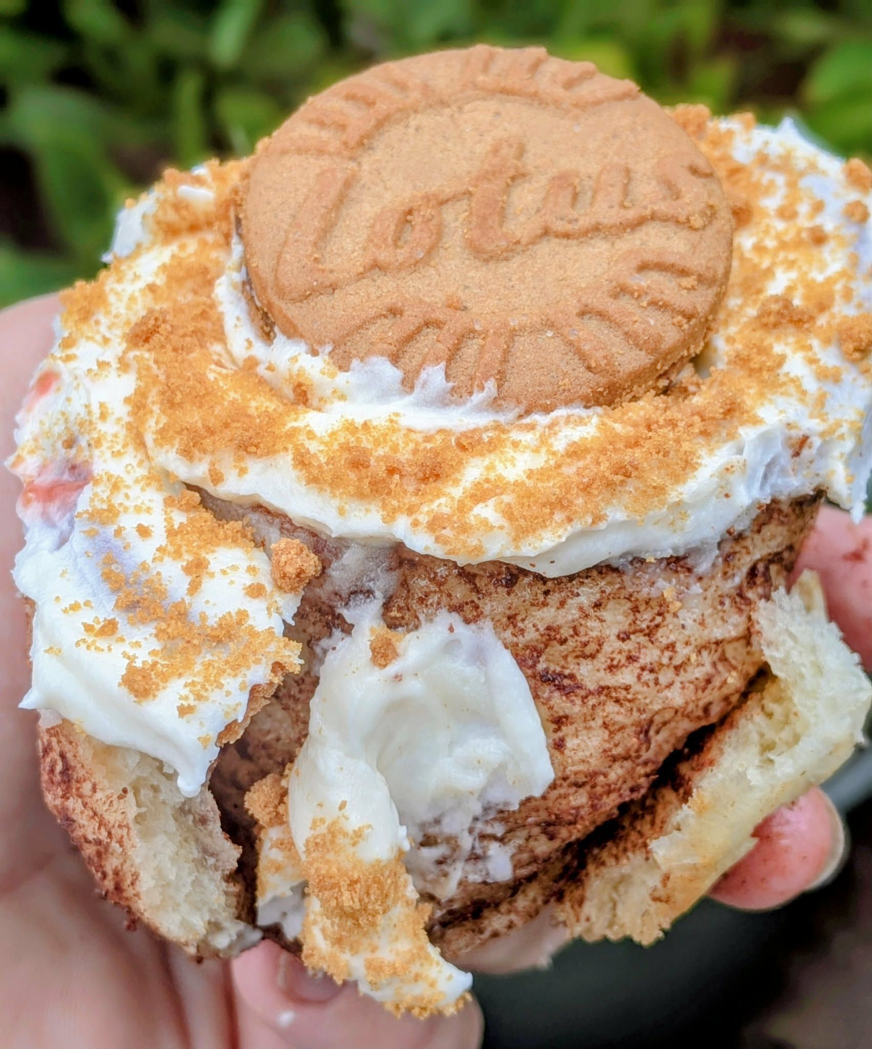 Close-up of a frosted cinnamon roll topped with a cookie and cookie crumbs.