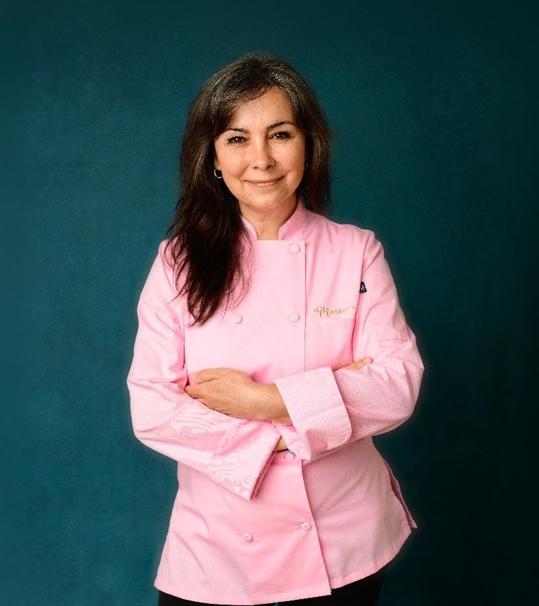 Woman in pink chef coat with crossed arms, turquoise background.