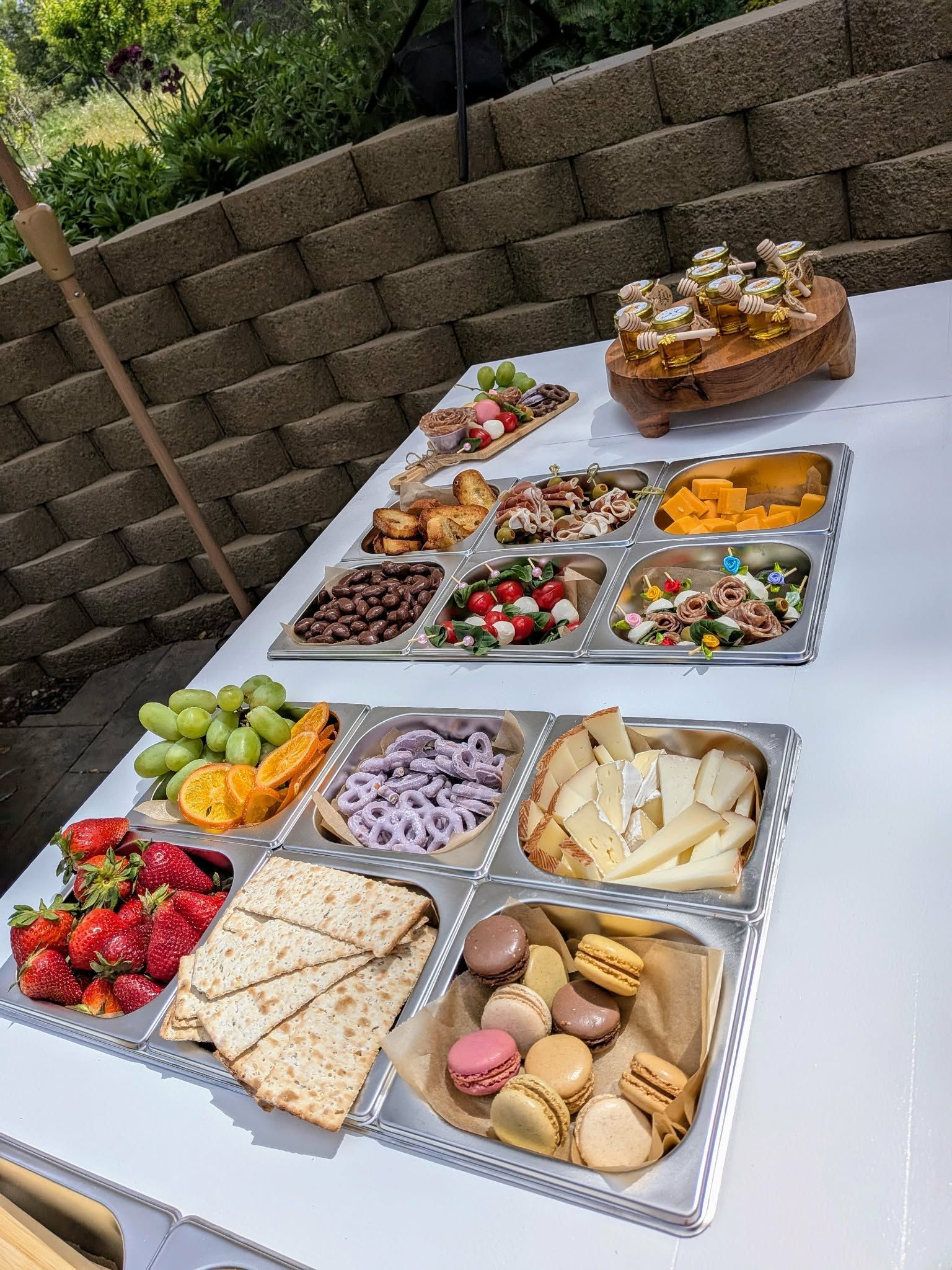 Buffet table with assorted foods: fruit, vegetables, baked goods, and cheese, outdoors.