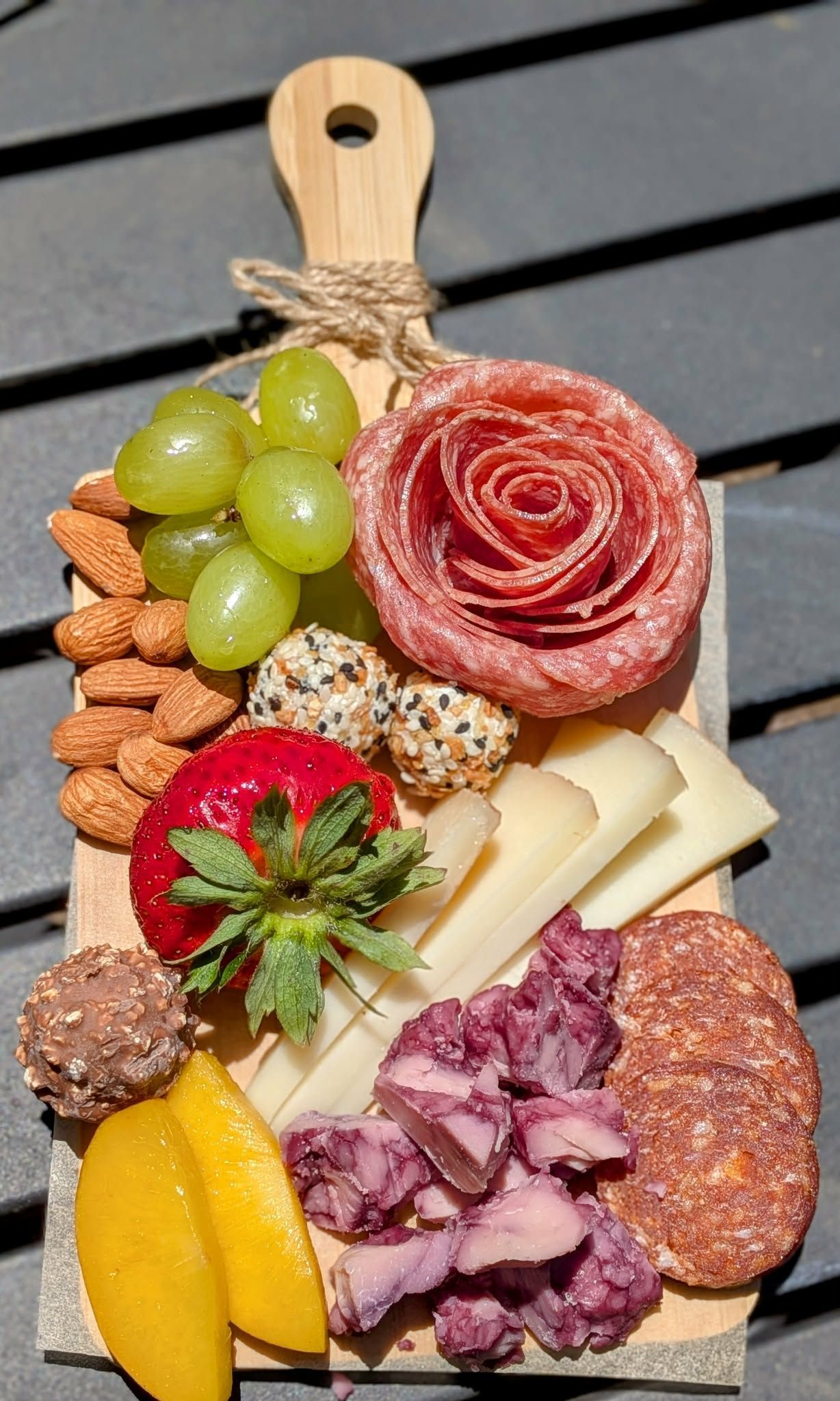 Charcuterie board with grapes, nuts, cheese, salami rose, and other snacks on wooden board.