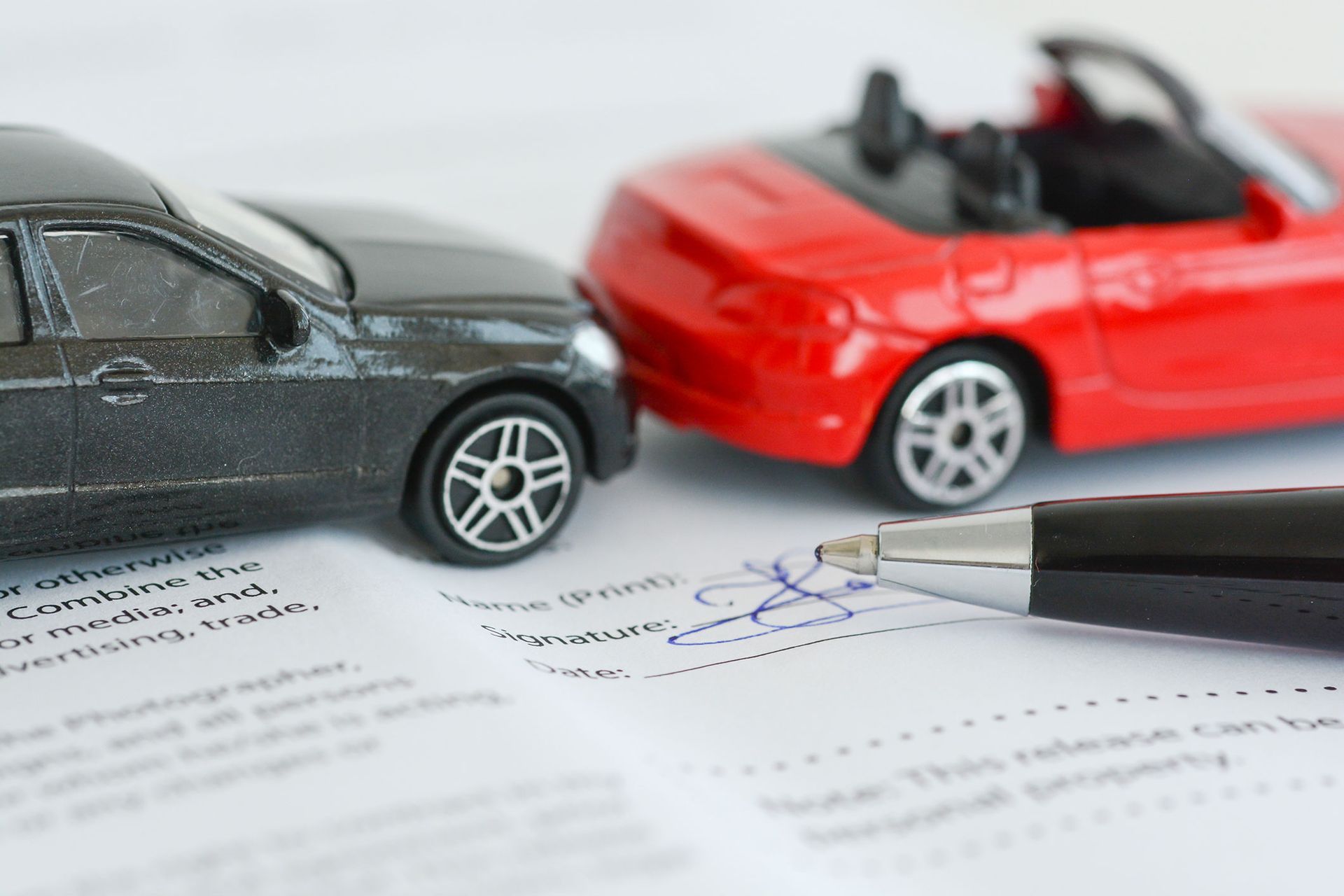 Toy cars in collision over a document; pen poised to sign release.