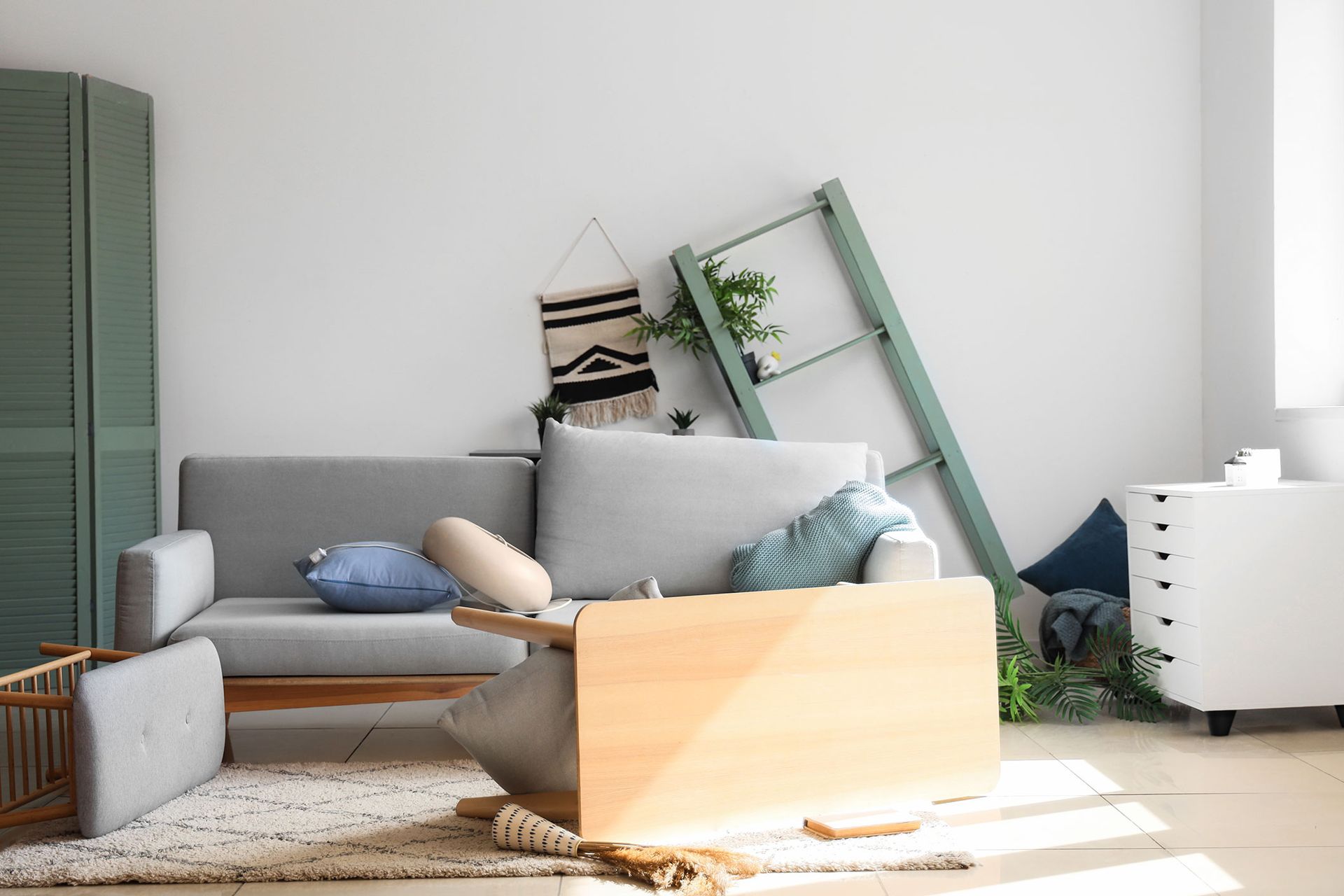 A room in disarray: couch with pillows, fallen plant stand, and overturned table.