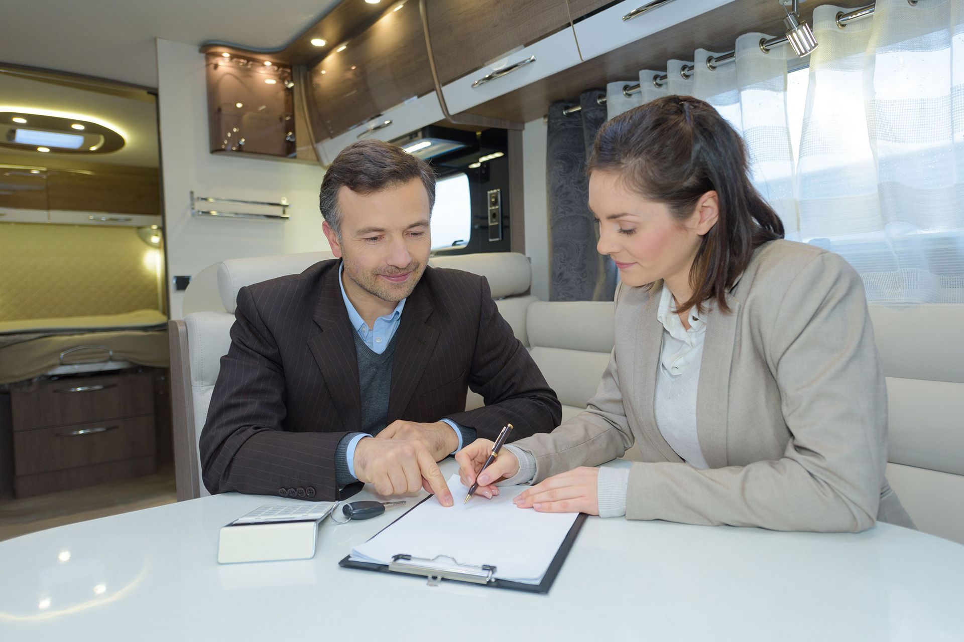 Man and woman in an RV, looking at papers on a table, signing documents.