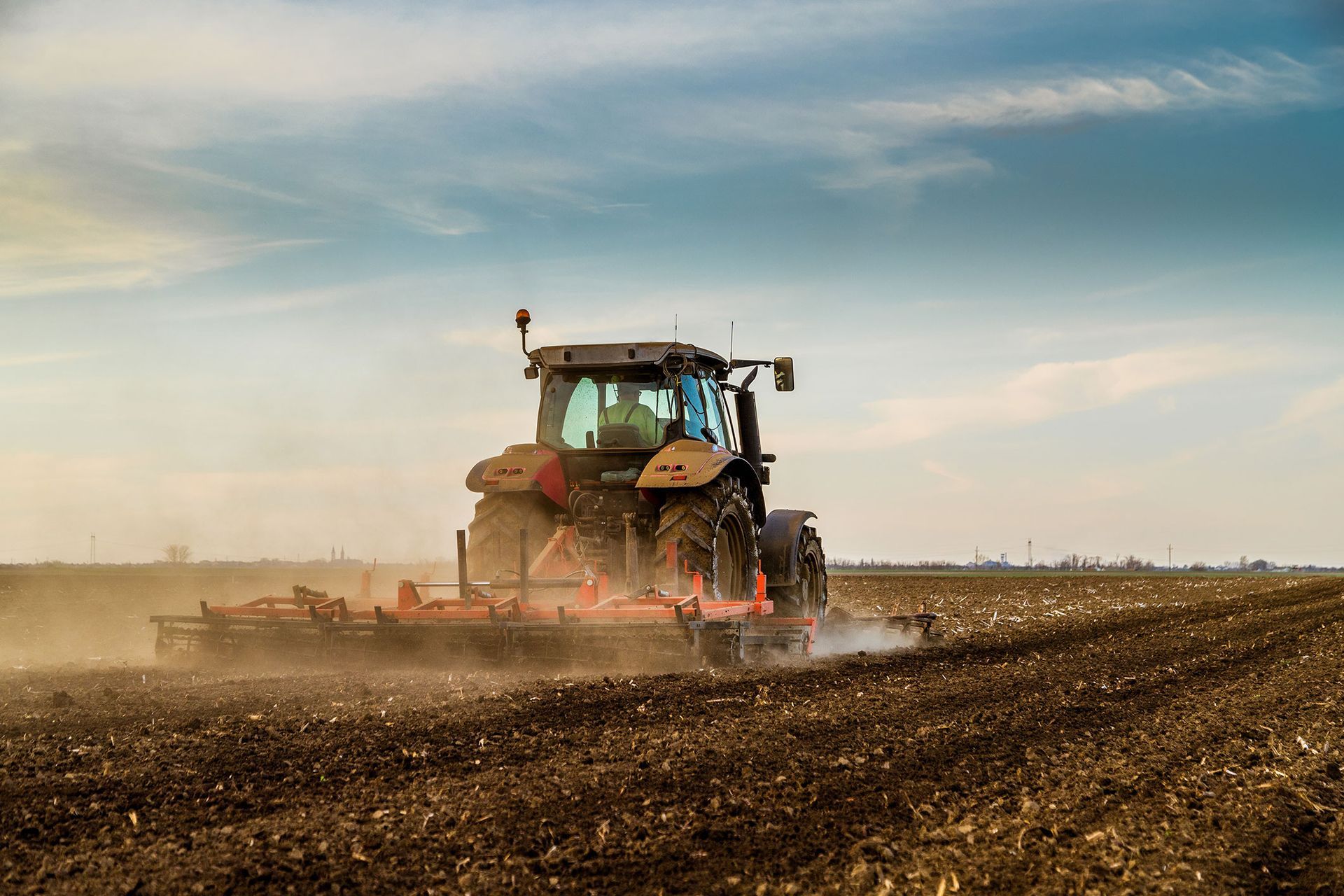 Tractor plowing a field, kicking up dust under a cloudy sky.