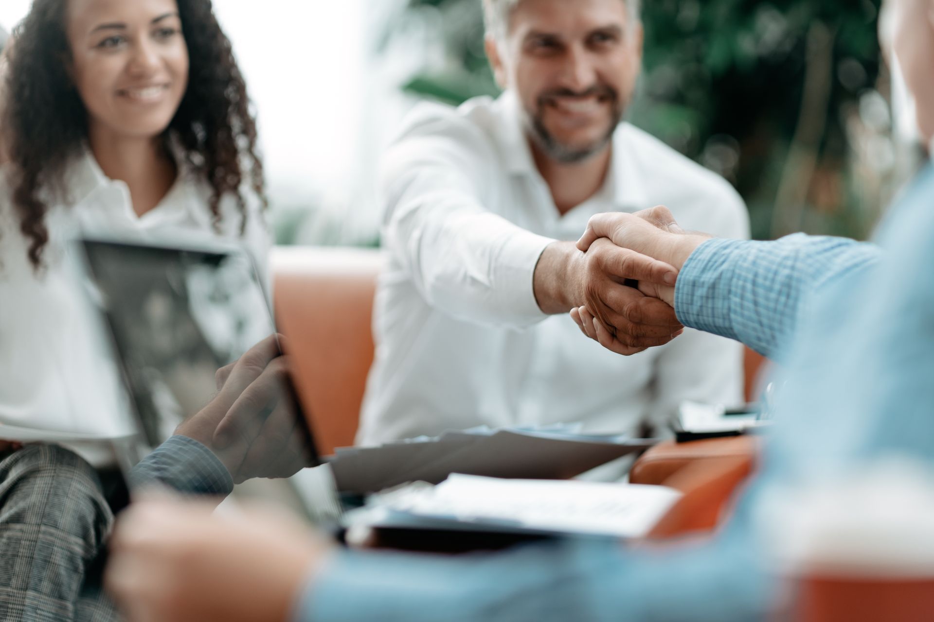 People in a meeting shaking hands across a table with documents and a laptop.