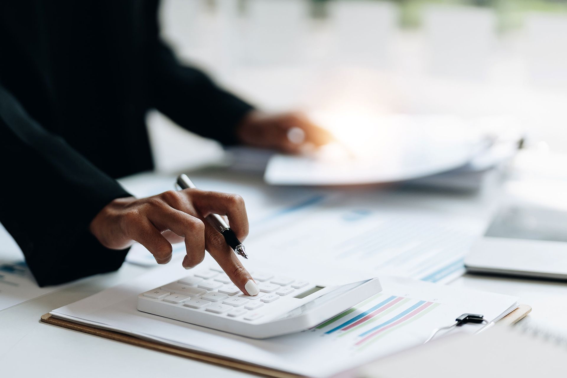 Person's hands using a calculator, with papers and a pen on a desk.