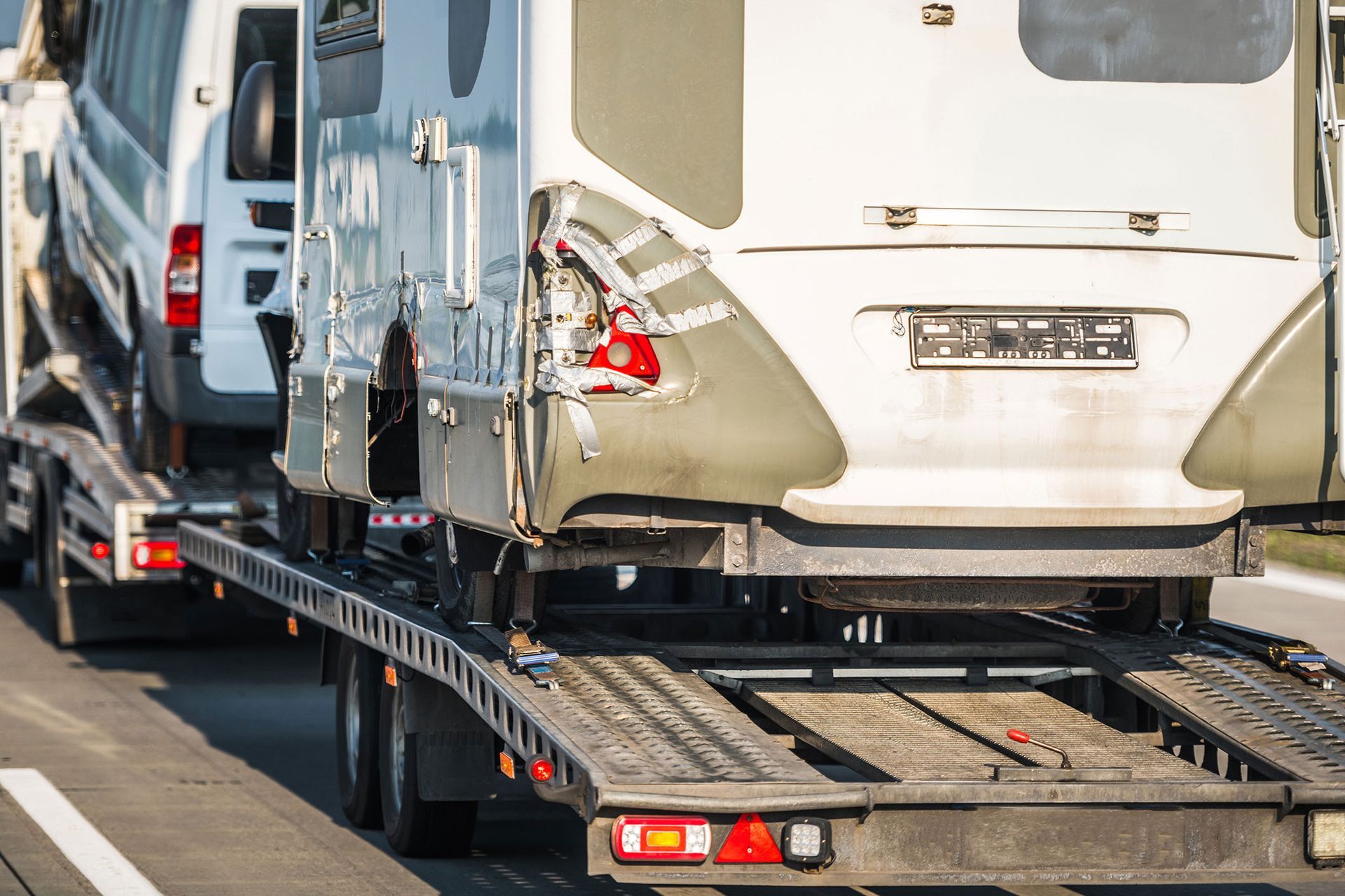Vehicles on a flatbed trailer traveling on a highway. The vehicles include a camper and a van.