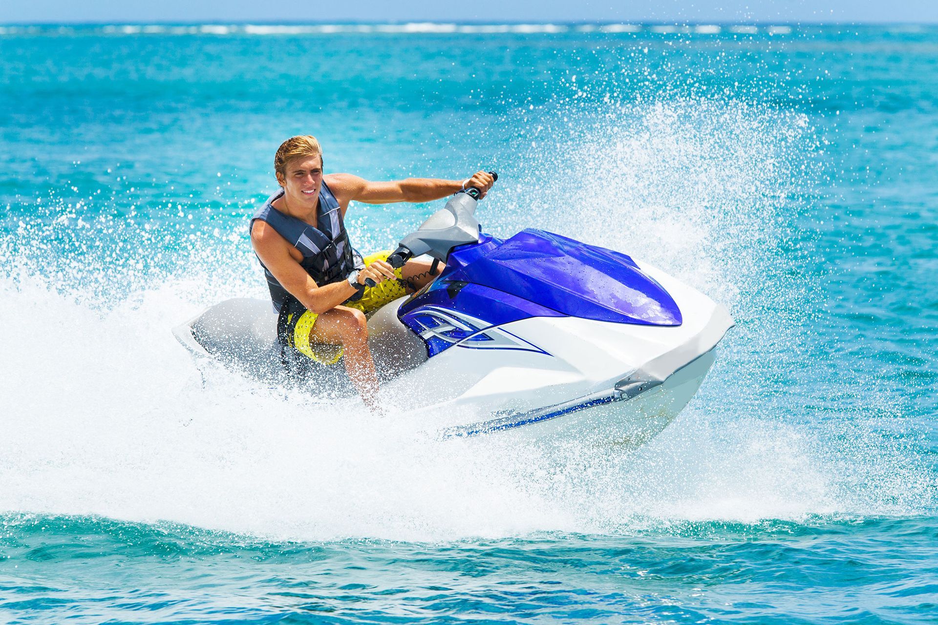 Man on a jet ski in blue water, spraying water; sunny day.
