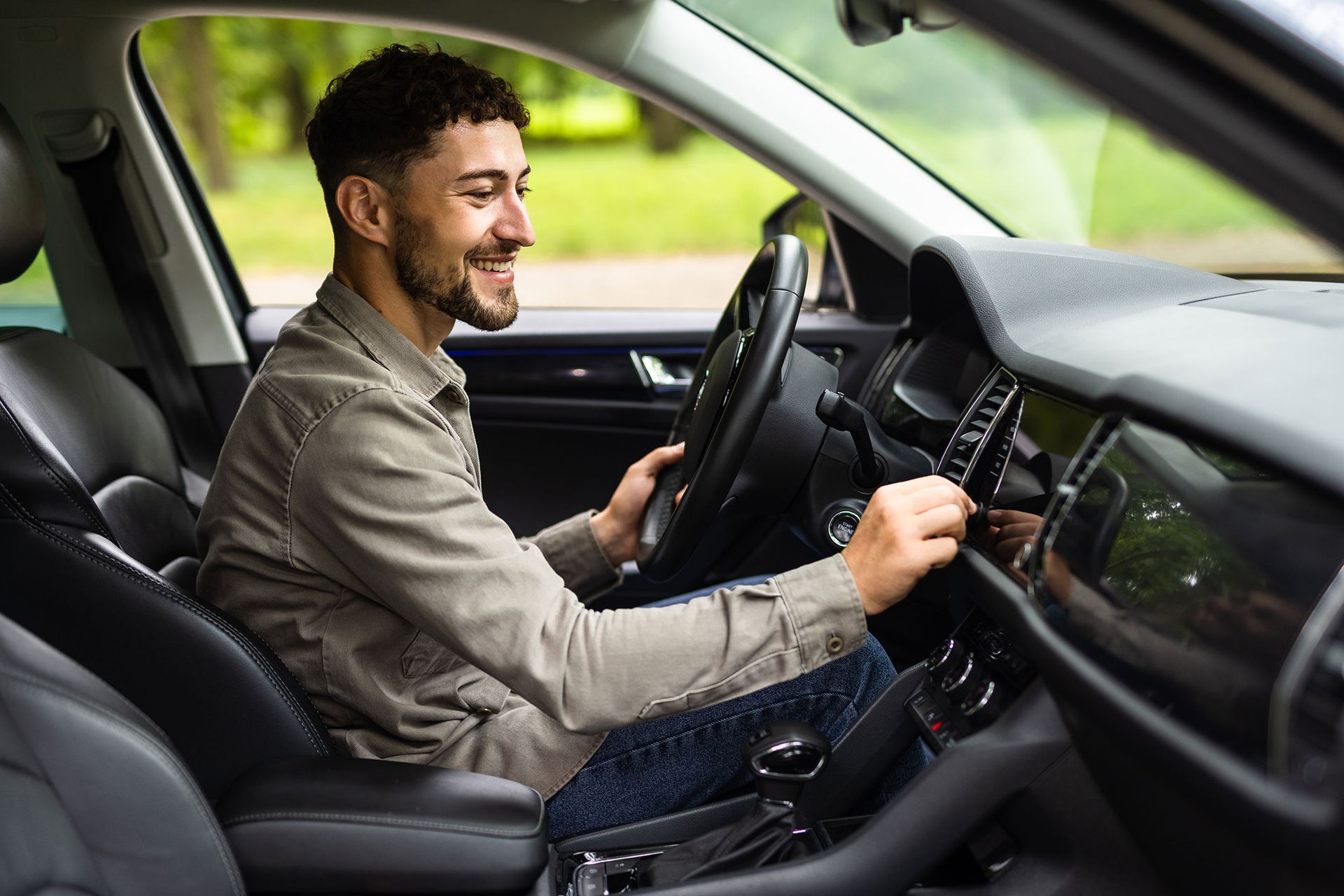 Man in a car, smiling, adjusting dashboard controls.