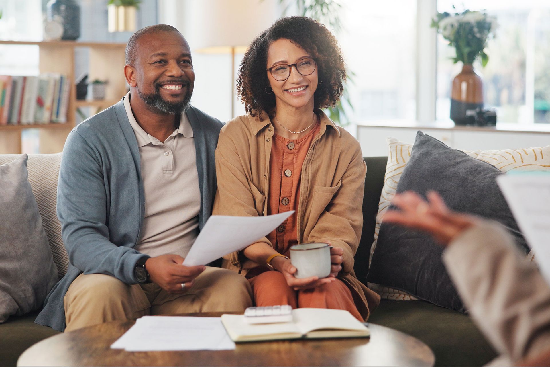 Couple smiling, looking at papers, meeting with someone on a couch.
