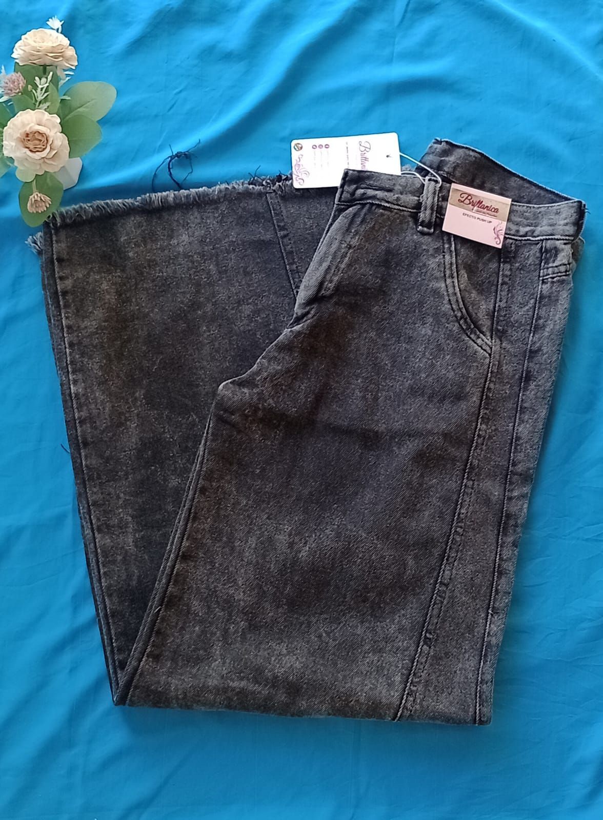 Un par de pantalones vaqueros de mezclilla color carbón con efecto desteñido, pernera acampanada.