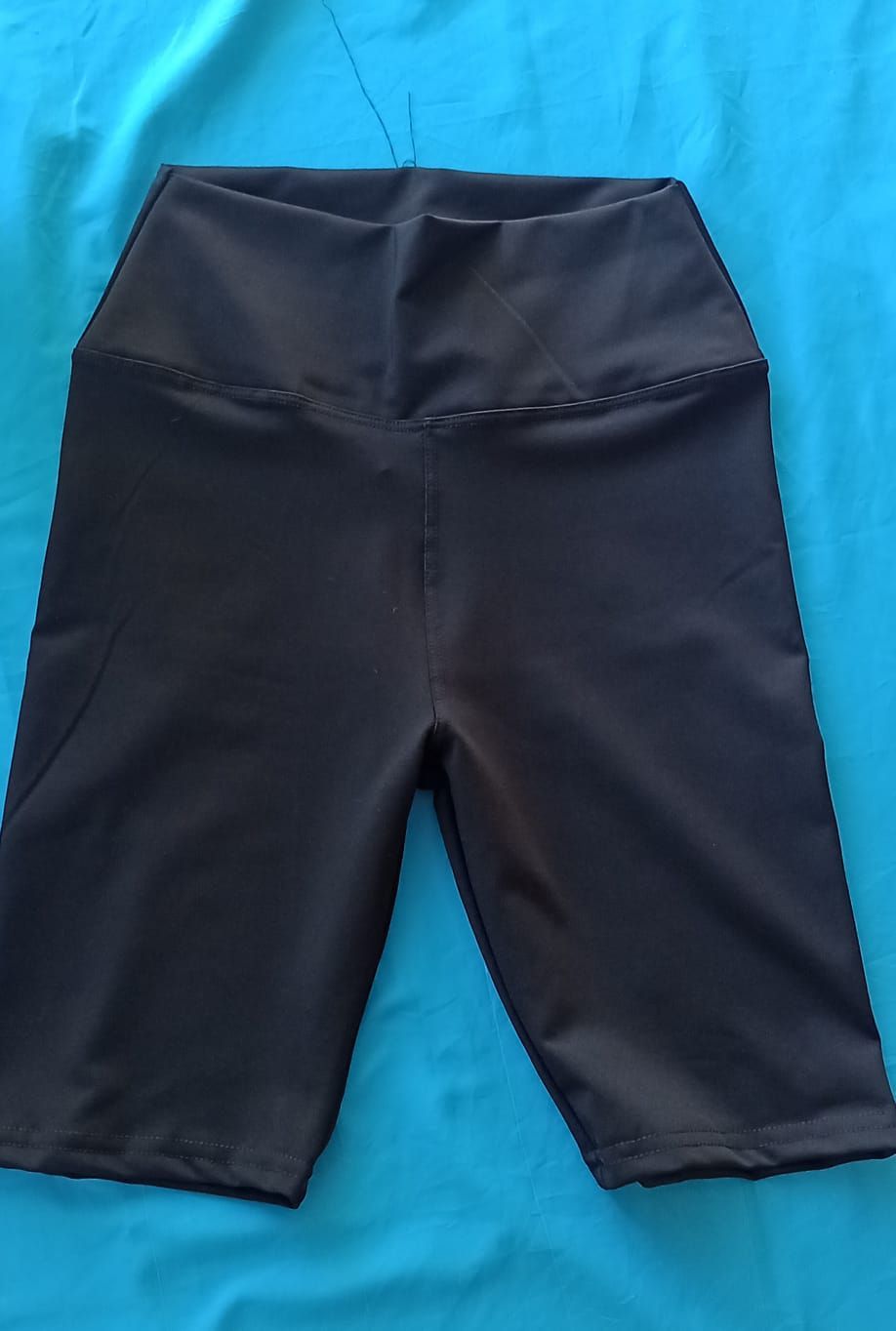 Pantalones cortos de ciclista negros de talle alto, exhibidos sobre un fondo azul brillante.