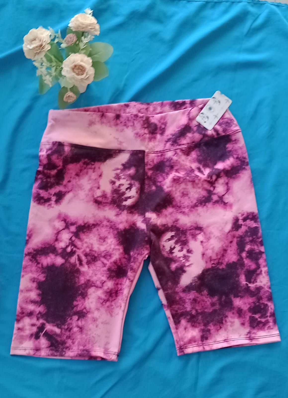 Pantalones cortos de ciclista con un estampado tie-dye en rosa y morado oscuro, mostrados extendidos.