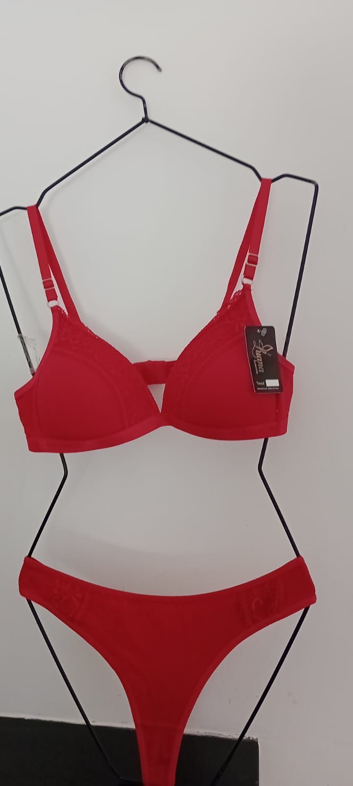 Un conjunto de sujetador y tanga de color rojo intenso cuelga de un maniquí de alambre sobre un fondo blanco liso.