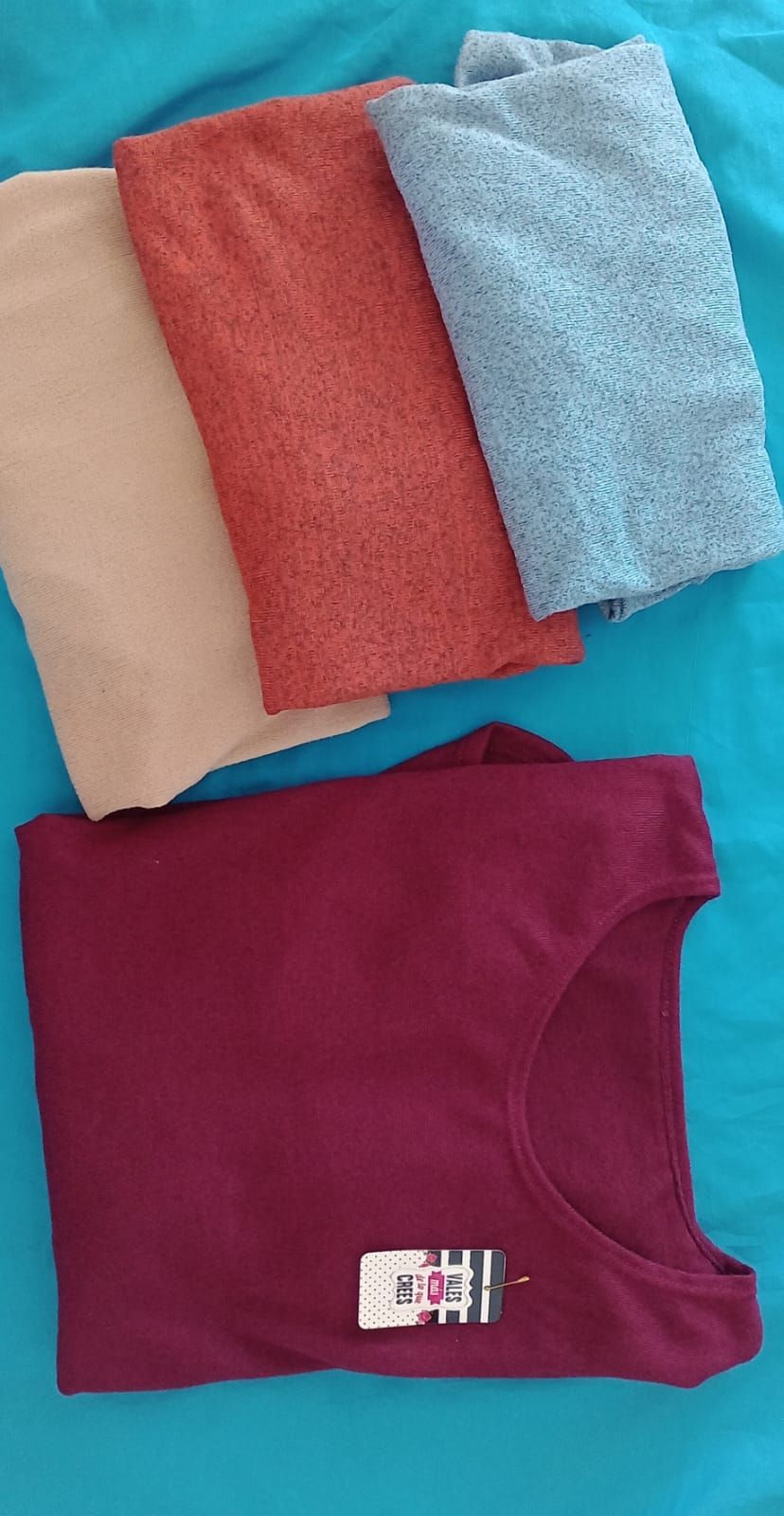 Una blusa de manga larga de color naranja óxido liso cuelga de una percha rosa sobre un fondo azul brillante.