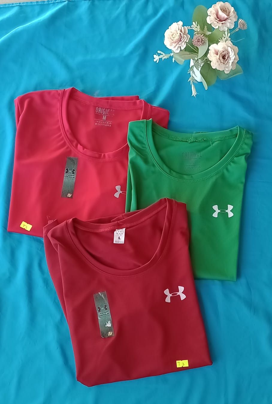 Una camiseta roja de manga corta de Under Armour con la etiqueta de la marca está extendida sobre una superficie azul.