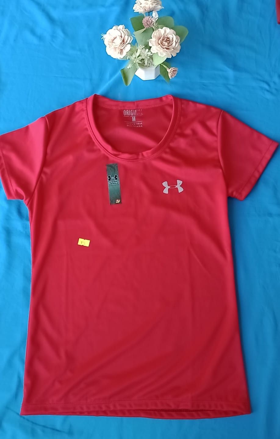 Una camiseta roja de manga corta de Under Armour con la etiqueta de la marca está extendida sobre una superficie azul.