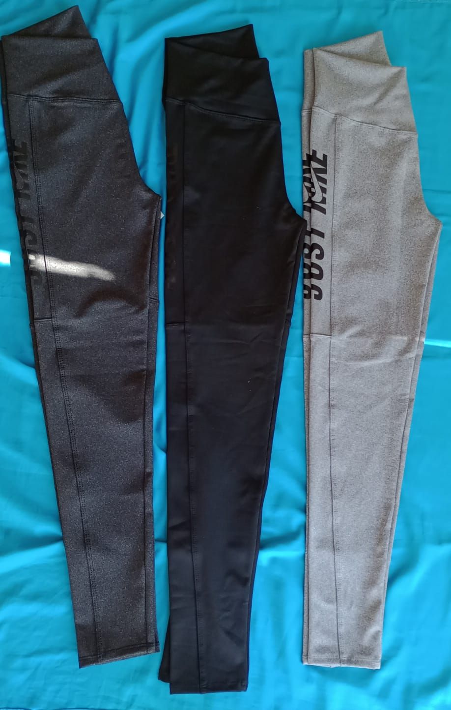 Leggings Nike de talle alto en color gris oscuro con el logotipo swoosh blanco, extendidos sobre una superficie azul.