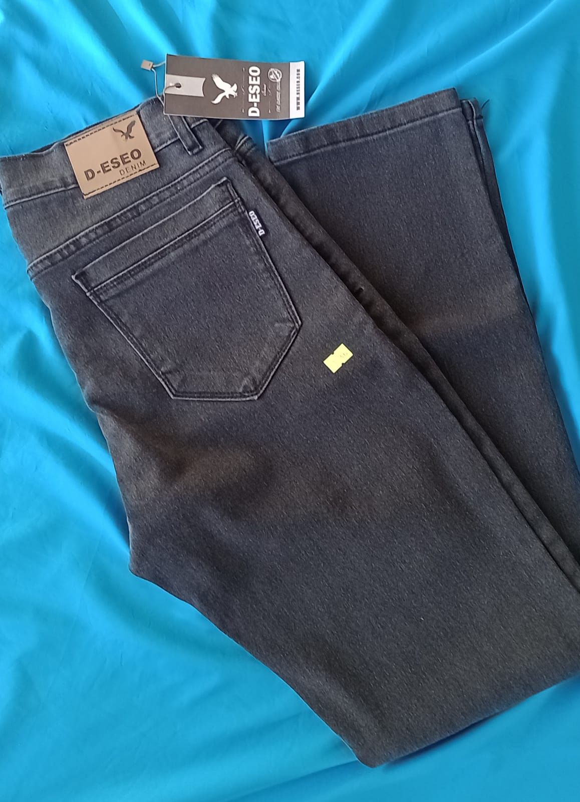 Un par de vaqueros de color carbón con etiqueta de cuero de marca y etiqueta colgante.