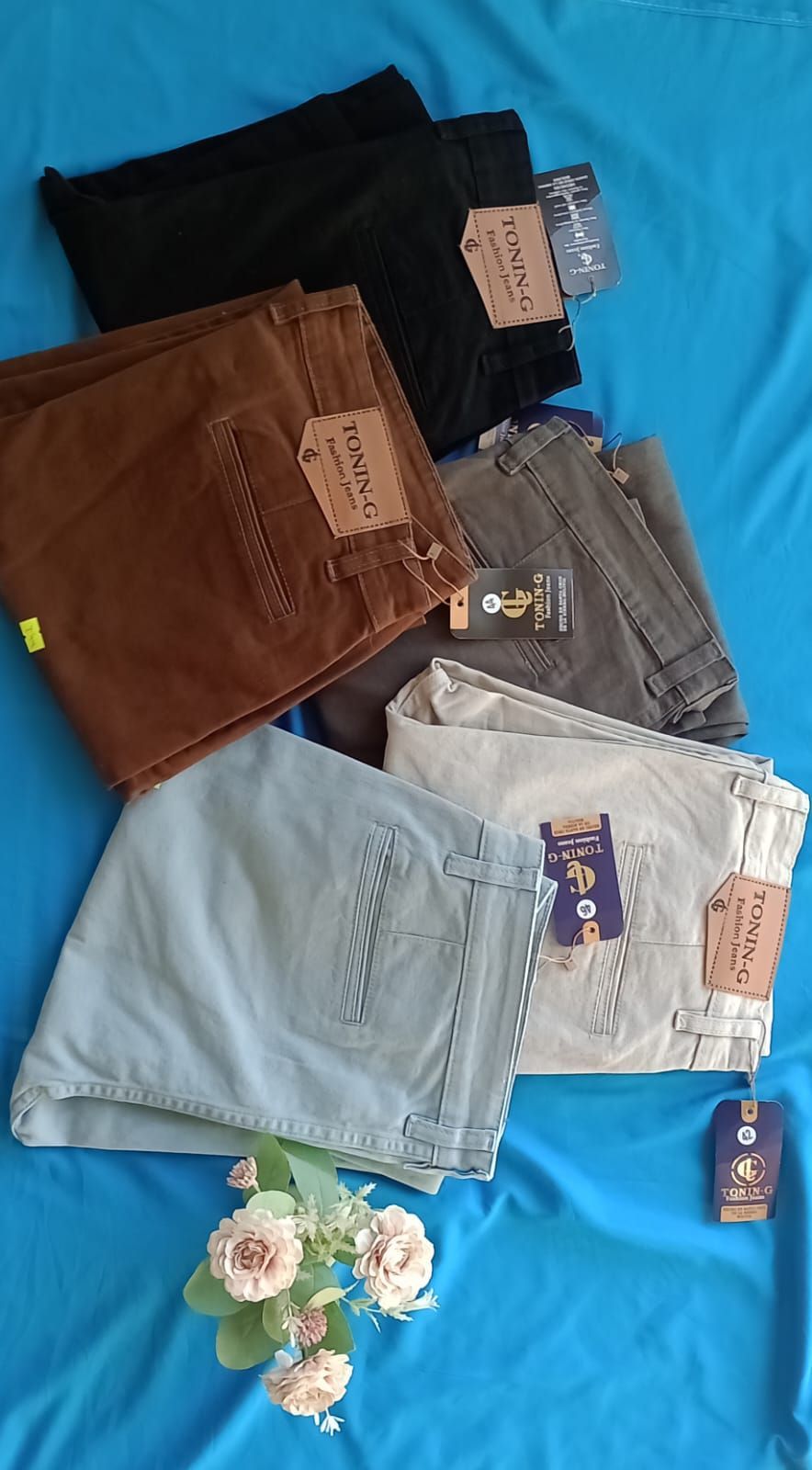 Un par de vaqueros negros con un parche de cuero marrón de la marca, extendidos sobre un fondo de tela azul.