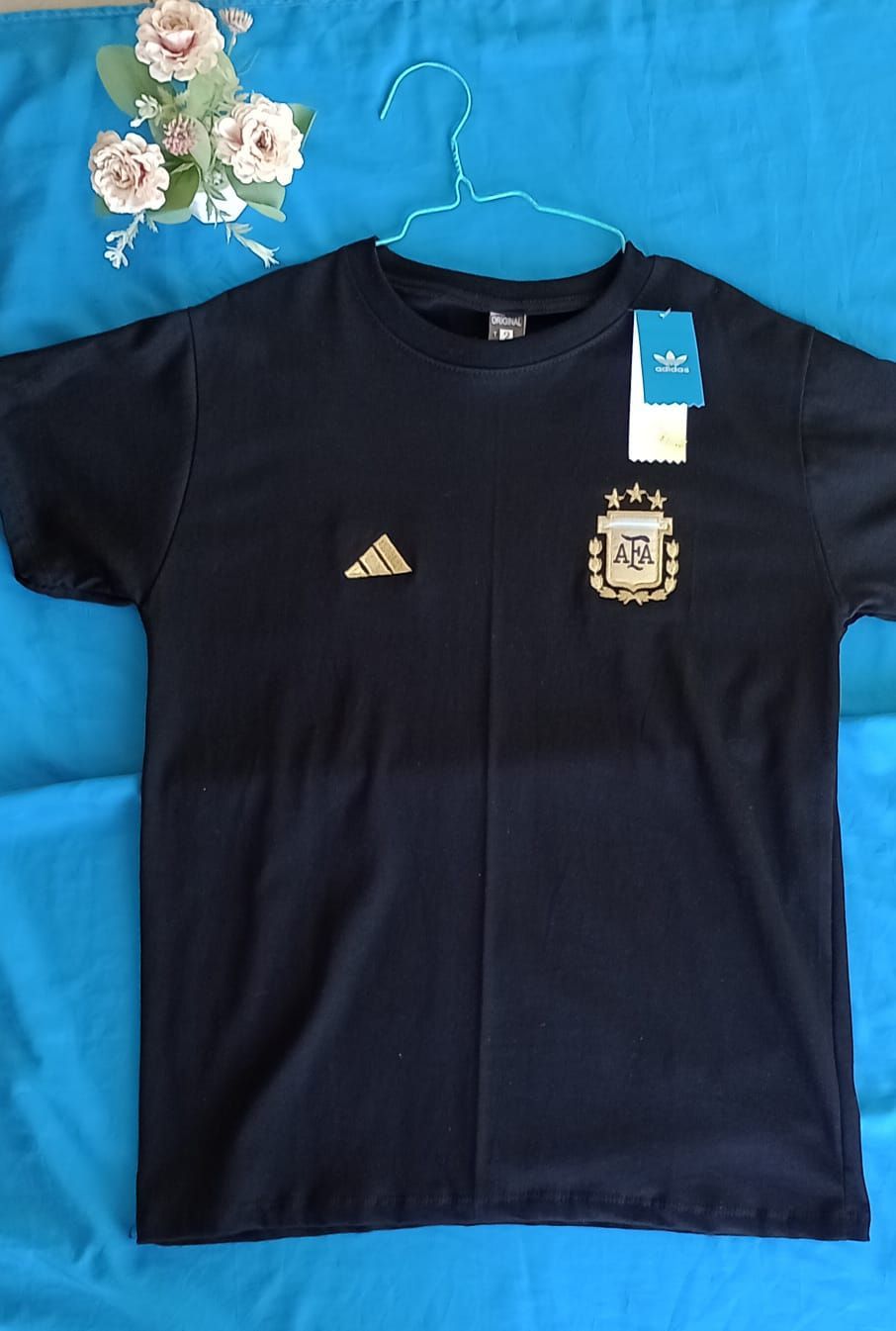 Una camiseta negra de manga corta con el logotipo dorado de Adidas y el escudo de la selección.