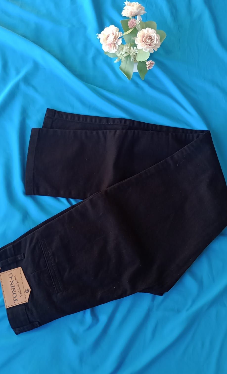 Un par de vaqueros negros con un parche de cuero marrón de la marca, extendidos sobre un fondo de tela azul.