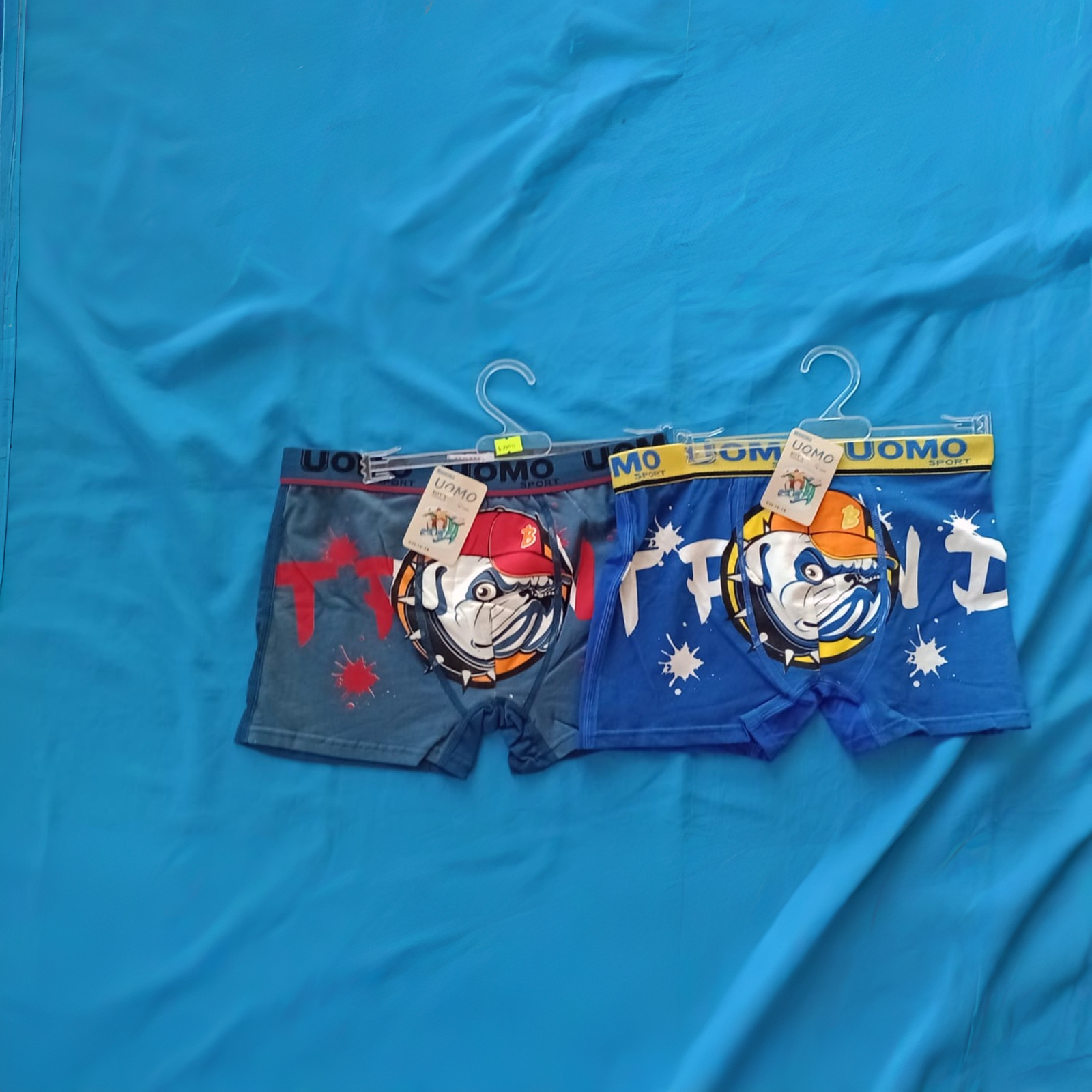 Dos pares de calzoncillos bóxer negros y grises colgados en perchas con dibujos de bulldogs.