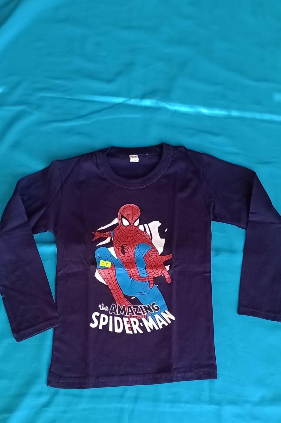 Una camisa azul oscuro de manga larga con un gráfico de Amazing Spider-Man sobre un fondo de tela turquesa.
