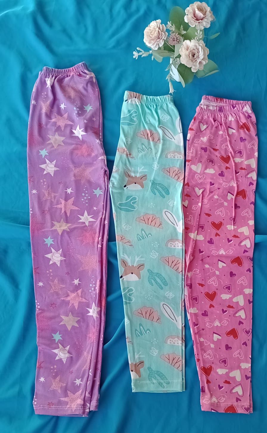 Tres pares de pantalones de pijama estampados en color morado, azul claro y rosa, extendidos sobre un fondo de tela azul.