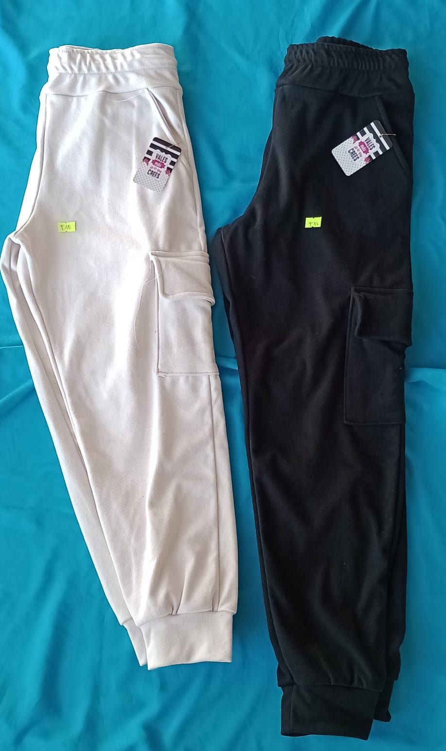 Pantalones cargo deportivos de color blanco roto con puños elásticos y bolsillos laterales sobre fondo azul.