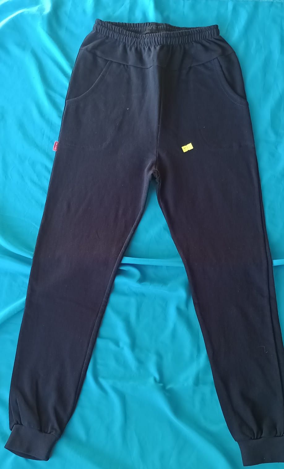 Dos pares de pantalones deportivos, uno azul marino y otro negro, extendidos sobre una superficie azul.