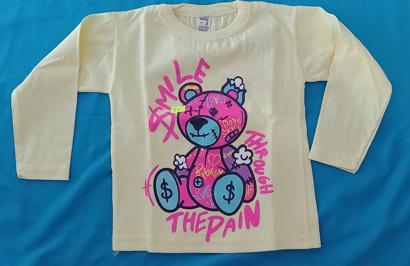 Una camiseta de manga larga color crema con un dibujo de un osito de peluche rosa con signos de dólar .