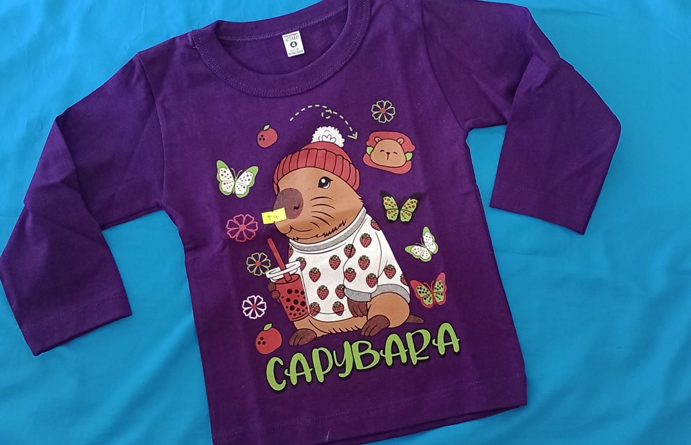 Una camiseta de manga larga color crema con un dibujo de un osito de peluche rosa con signos de dólar .