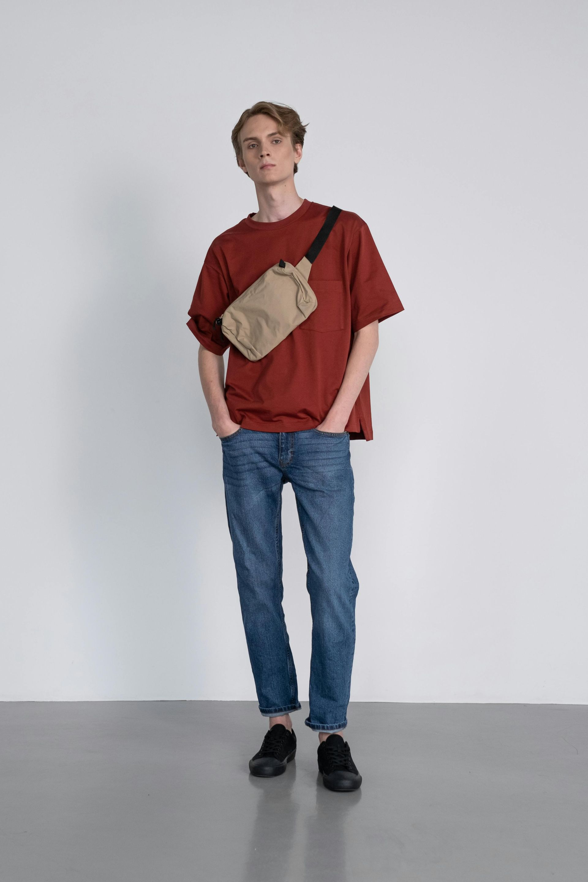 Una persona con una camiseta granate, vaqueros azules y zapatillas negras, que lleva un bolso cruzado.