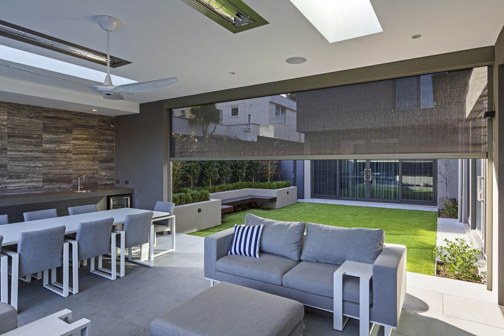 Outdoor living area with dining table, sofa, and lawn beyond a retractable shade.